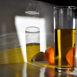 un vaso de aceite y una naranja organizados puesto sobre un rayo de sol que pasa por una ventana