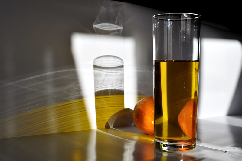 un vaso de aceite y una naranja organizados puesto sobre un rayo de sol que pasa por una ventana